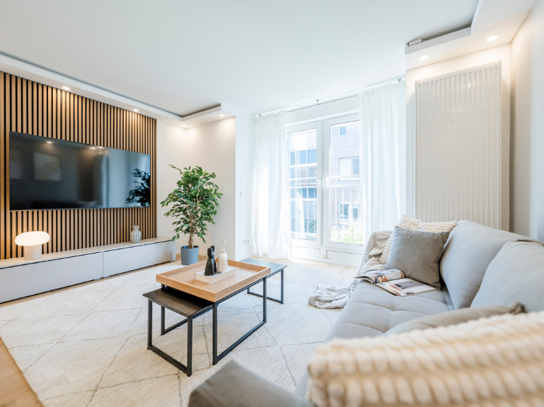 Modern eingerichtetes, möbliertes Apartment in Stuttgart mit hellem Wohnbereich, Sofa, TV-Wand mit Holzlamellen und Balkonzugang.