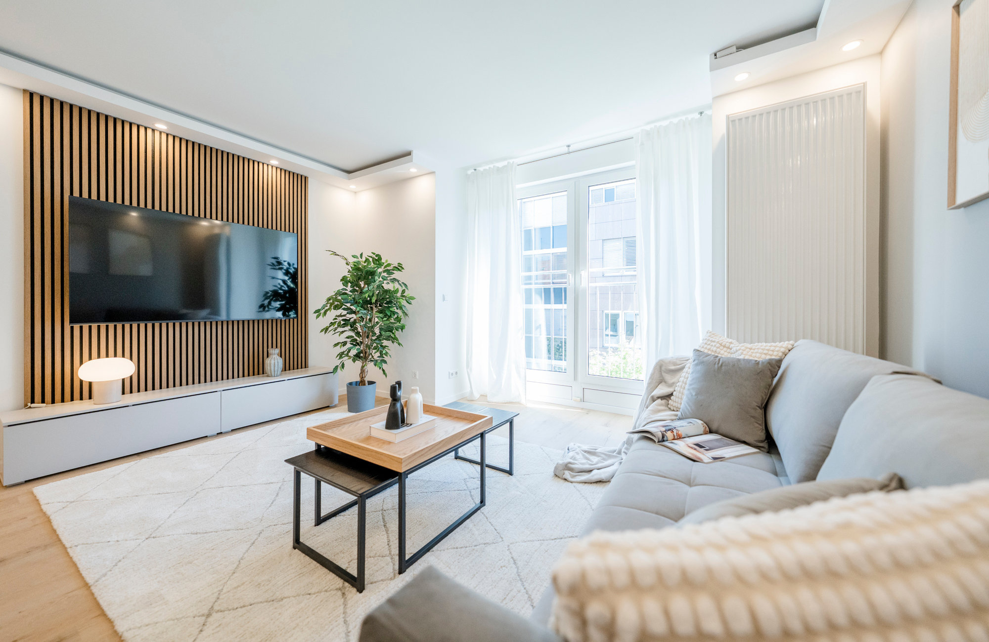 Modern eingerichtetes, möbliertes Apartment in Stuttgart mit hellem Wohnbereich, Sofa, TV-Wand mit Holzlamellen und Balkonzugang.